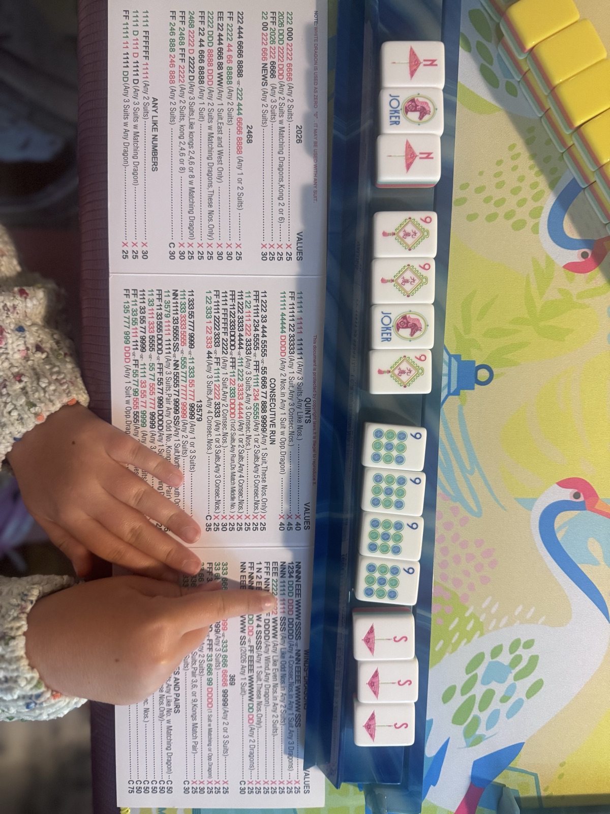 A young guest&rsquo;s hands arranging tiles beside the League card